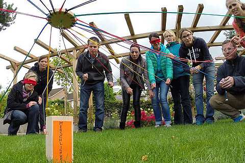 Aktive Menschen stellen beim TeamBuilding Holzklötze mit einem gemeinsamen Minikran aufeinander | mit GeccoTours-TeamEvents.com