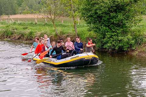 Eine Gruppe Menschen in einem Schlauchboot sitzend paddelt auf der Niers | mit GeccoTours-TeamEvents.com